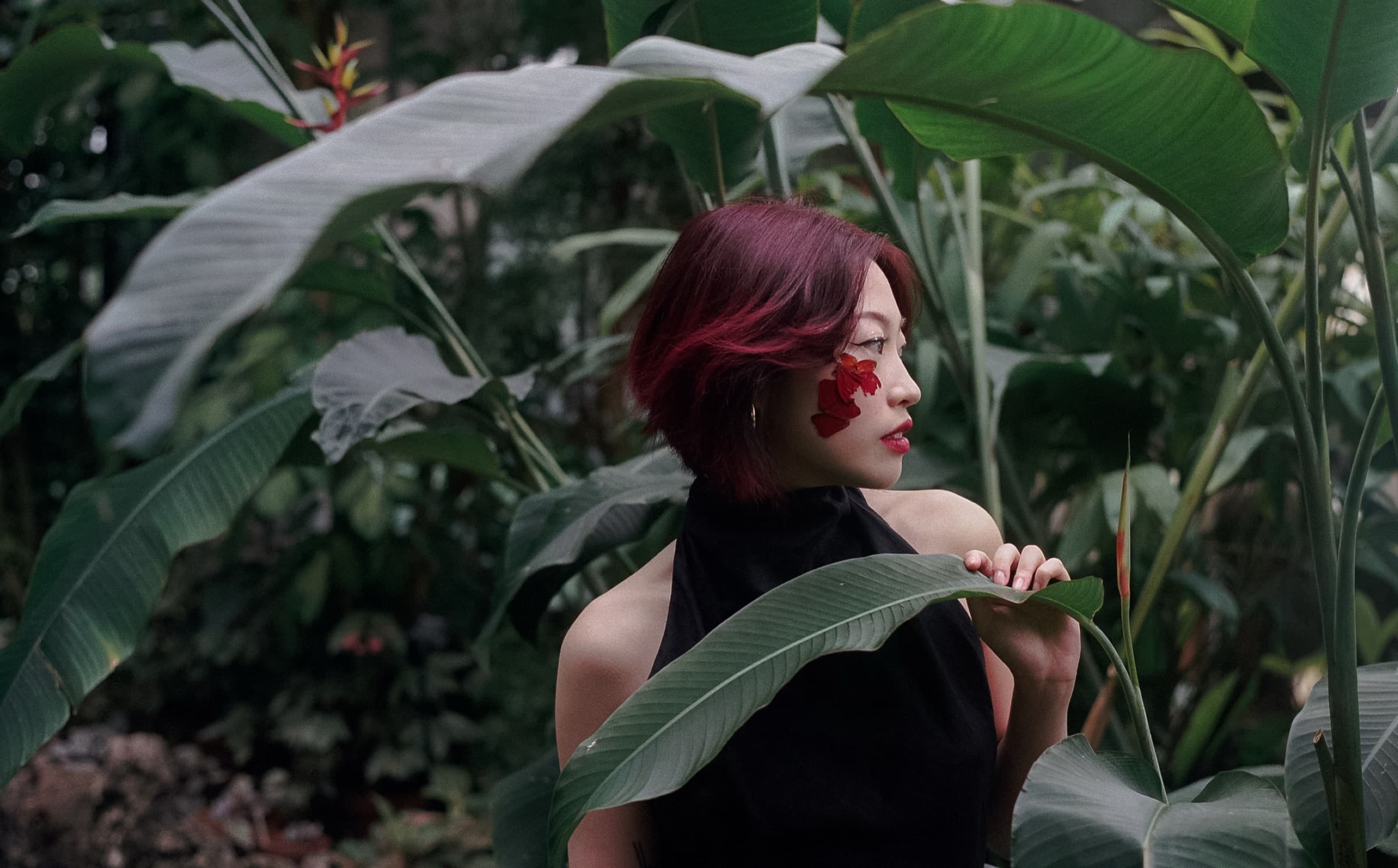 Portrait among broad banana leaves, red butterfly wings applied beneath the eye