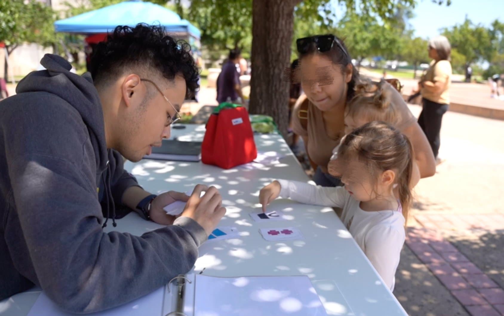 A researcher runs the card task at an outdoor table with a parent and child at the science museum
