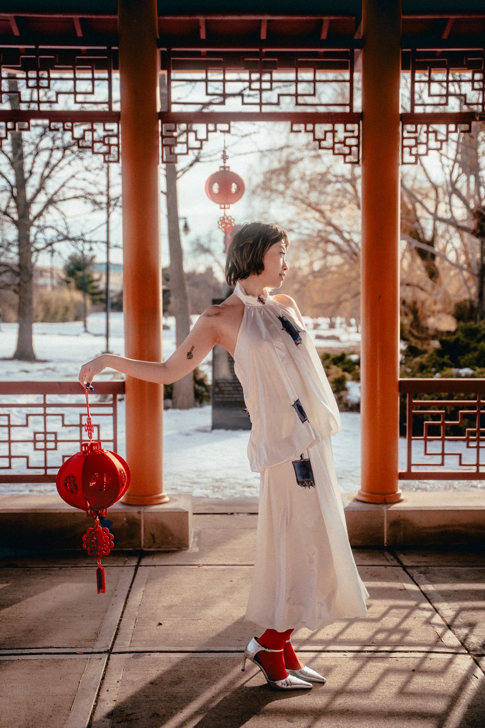 Standing in a red pavilion in winter, holding a red lantern out at arm's length