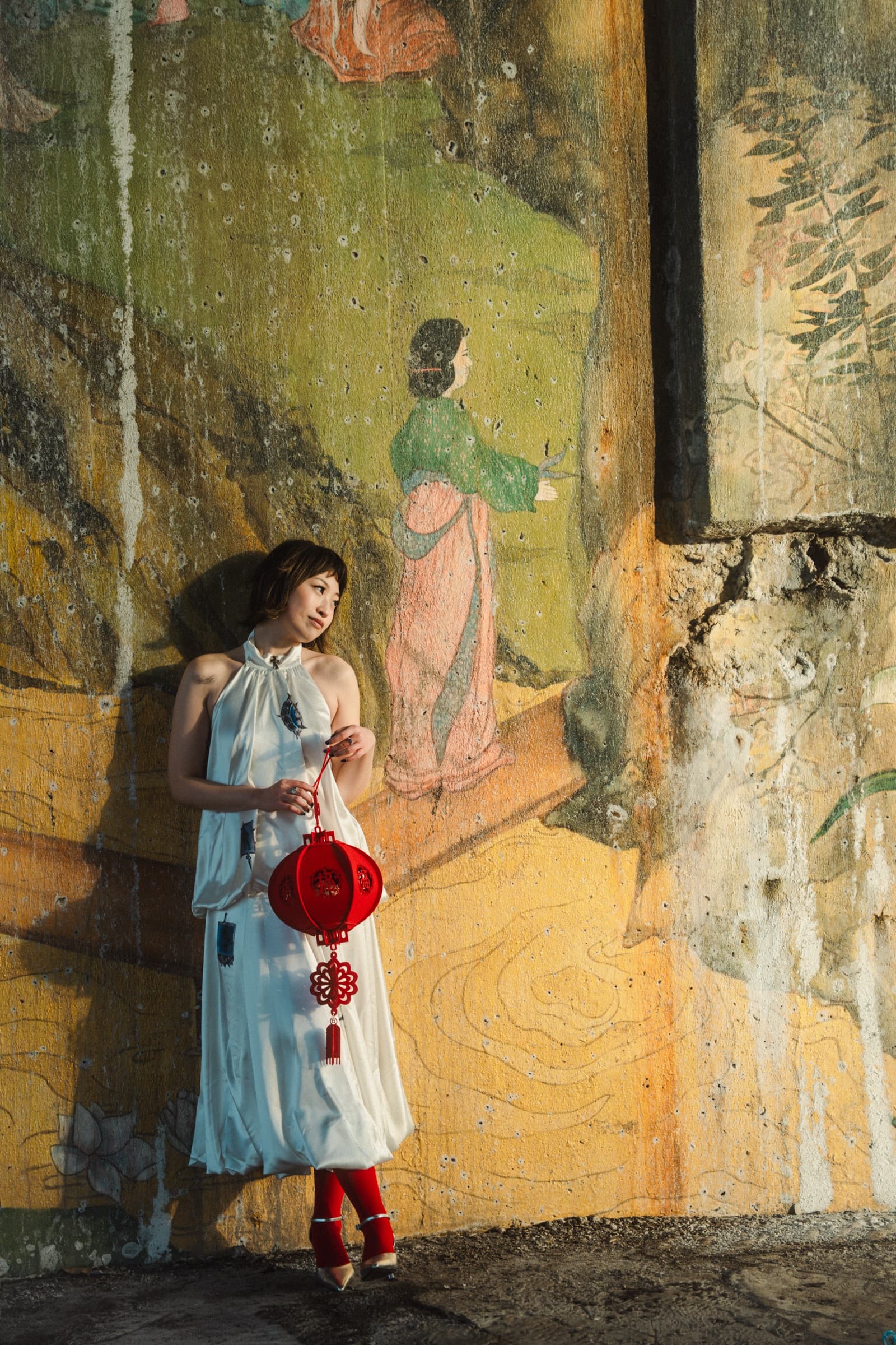 Standing against a weathered painted mural of a figure in a landscape