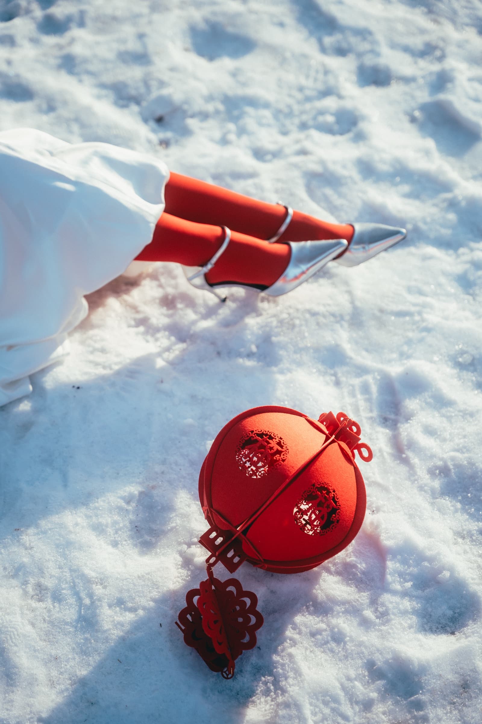 The lantern resting in the snow beside red stockings and silver heels